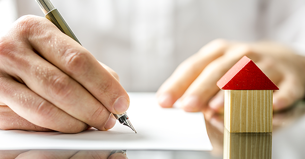 Transfer of Equity Process from Parachute Law: A man's hand signs a document beside a child's woodblock toy of a house with a red roof.
