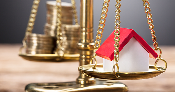 What is a Third Party Legal Charge? A guide from SAM Conveyancing. A model house sits on brass scales opposite a stack of coins