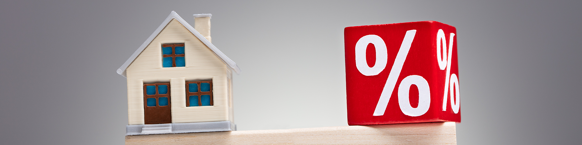 Beneficial Interest in Property from Parachute Law: a model house and a square block which reads '%' sit atop a long children's playing block, in balance on a cylindrical block