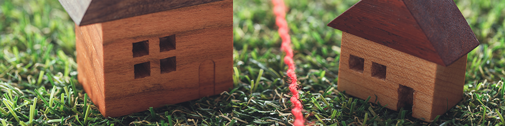 Boundary Dispute from Parachute Law: Two children's wood block toy houses sit on false grass, separated by a line of red string.