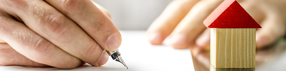 Transfer of Equity Process from Parachute Law: A man's hand signs a document beside a child's woodblock toy of a house with a red roof.